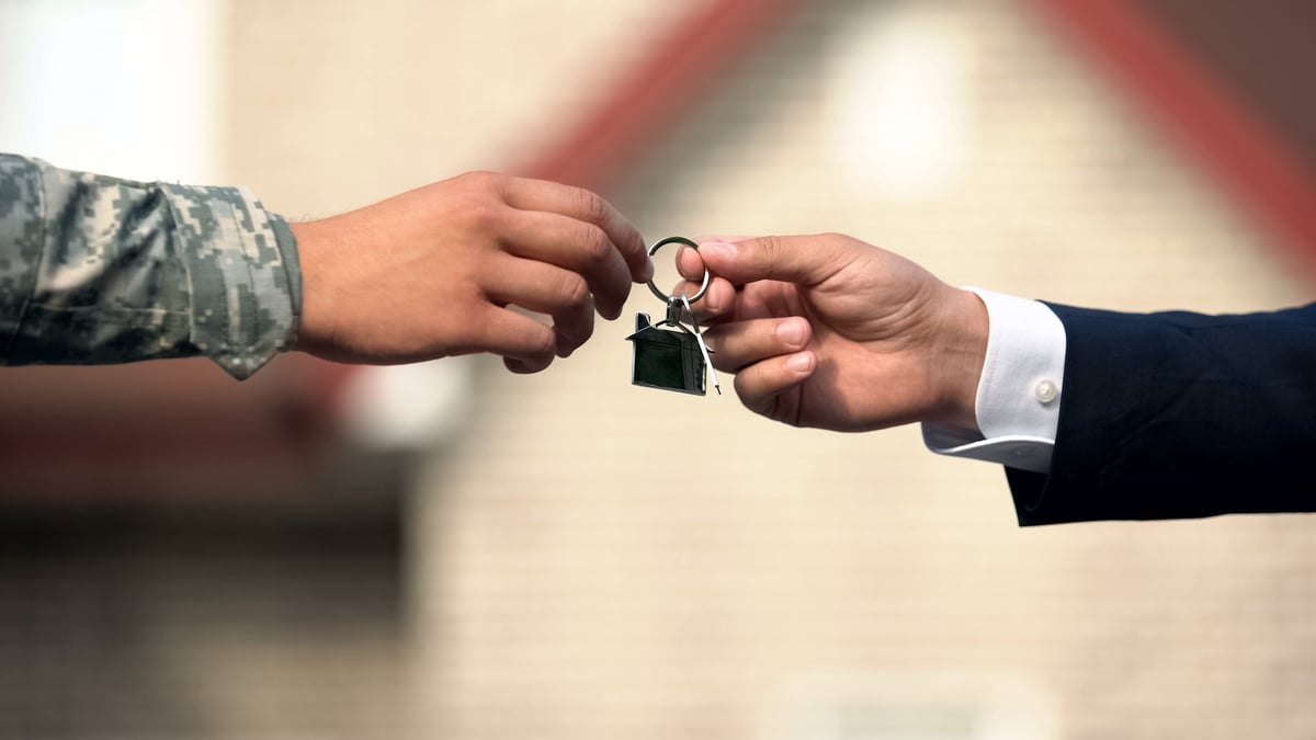 A housing navagator handing house keys to a Veteran in uniform, signifying a new home