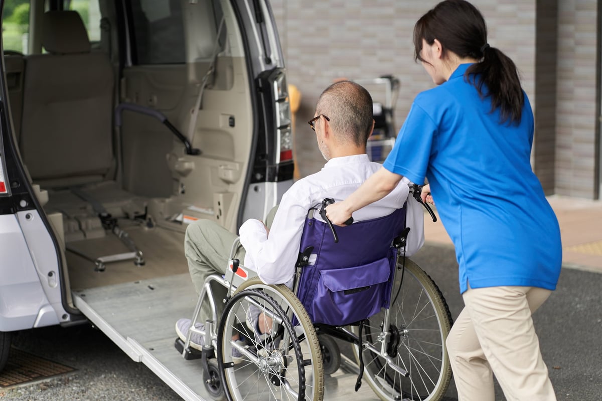 A caregiver assisting an elderly person into a non-emergency medical transport vehicle