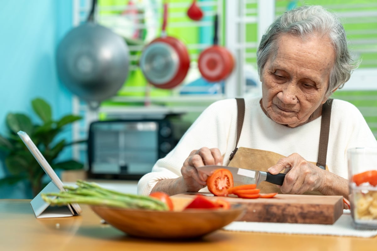 A senior woman independently preparing a meal in her own home kitchen